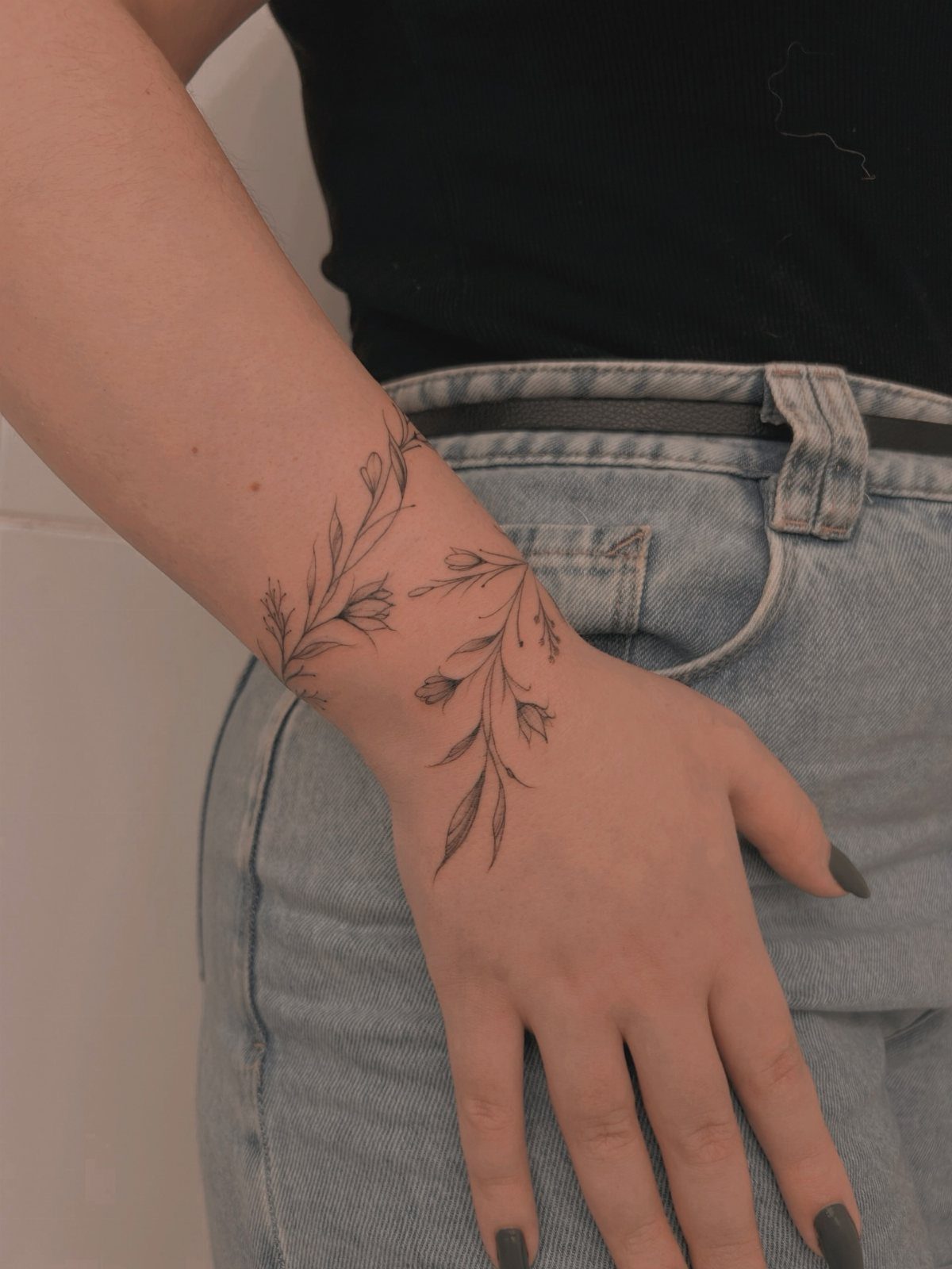 Fine line leaf tattoo on a woman's wrist and hand over blue jeans