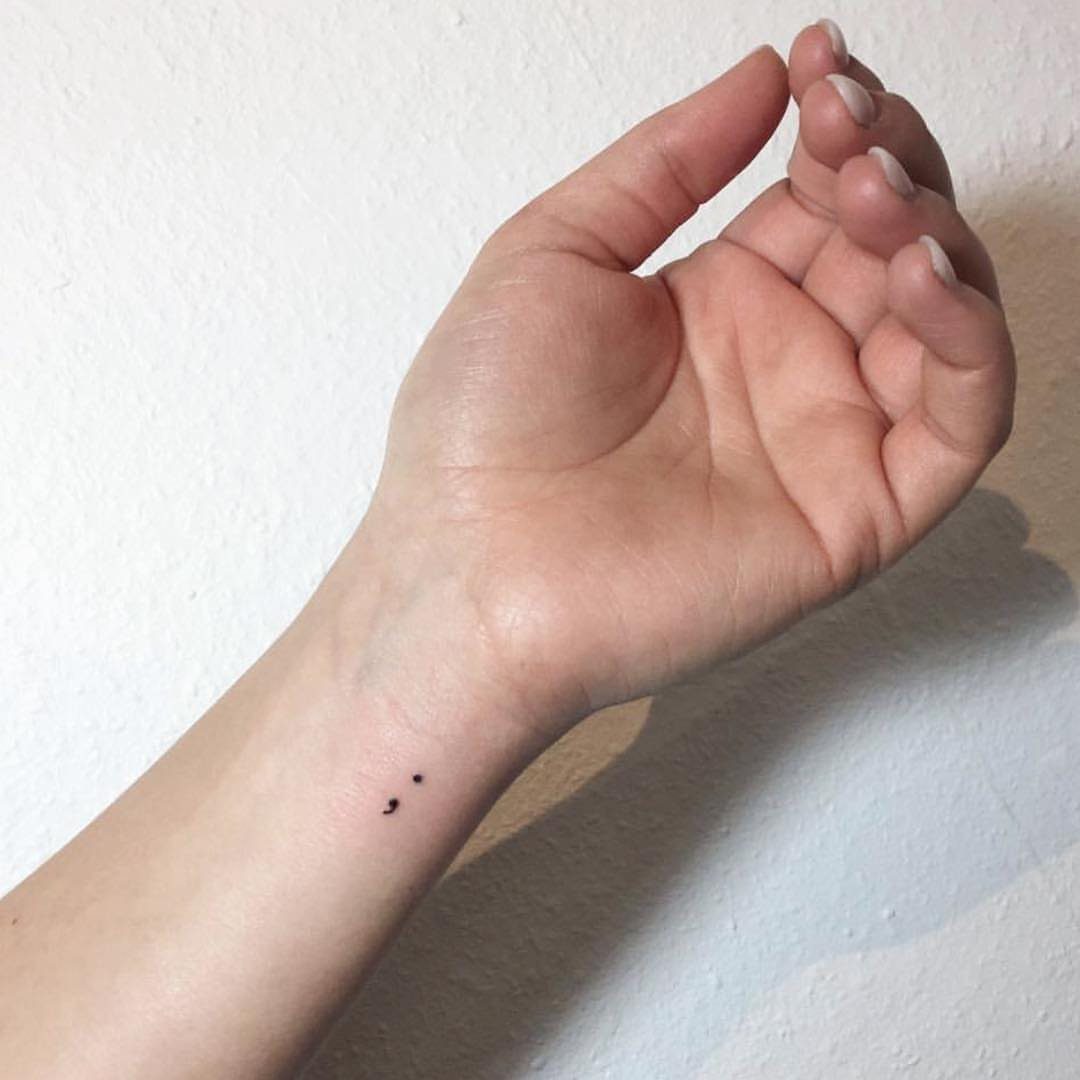 Semicolon tattoo on a person's inner wrist against a white background.