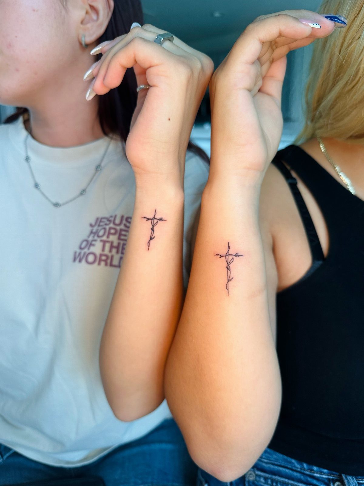 Two women's wrists with small black cross tattoos featuring delicate vine details.