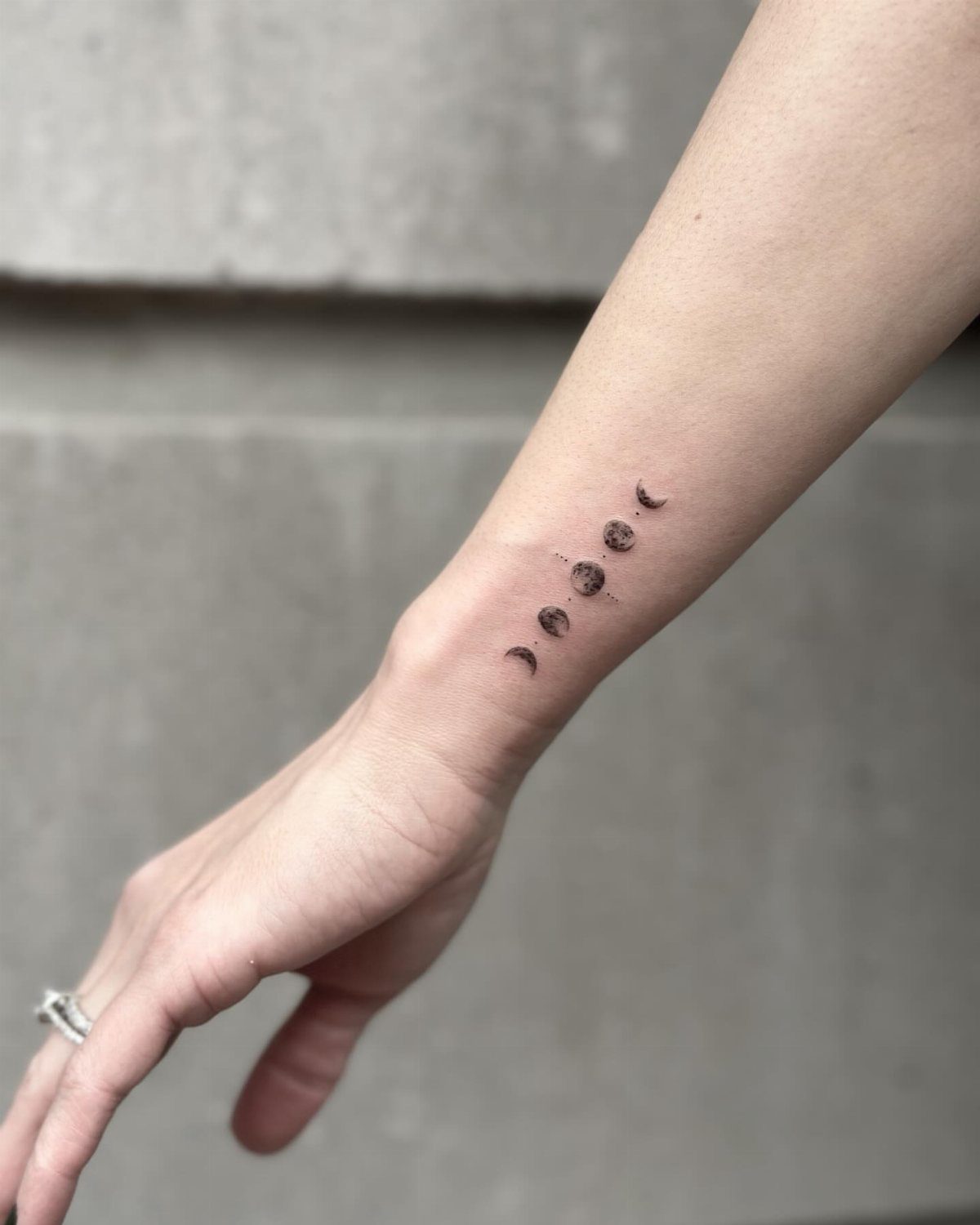 Moon phase tattoos on a person's inner wrist in small black ink designs.